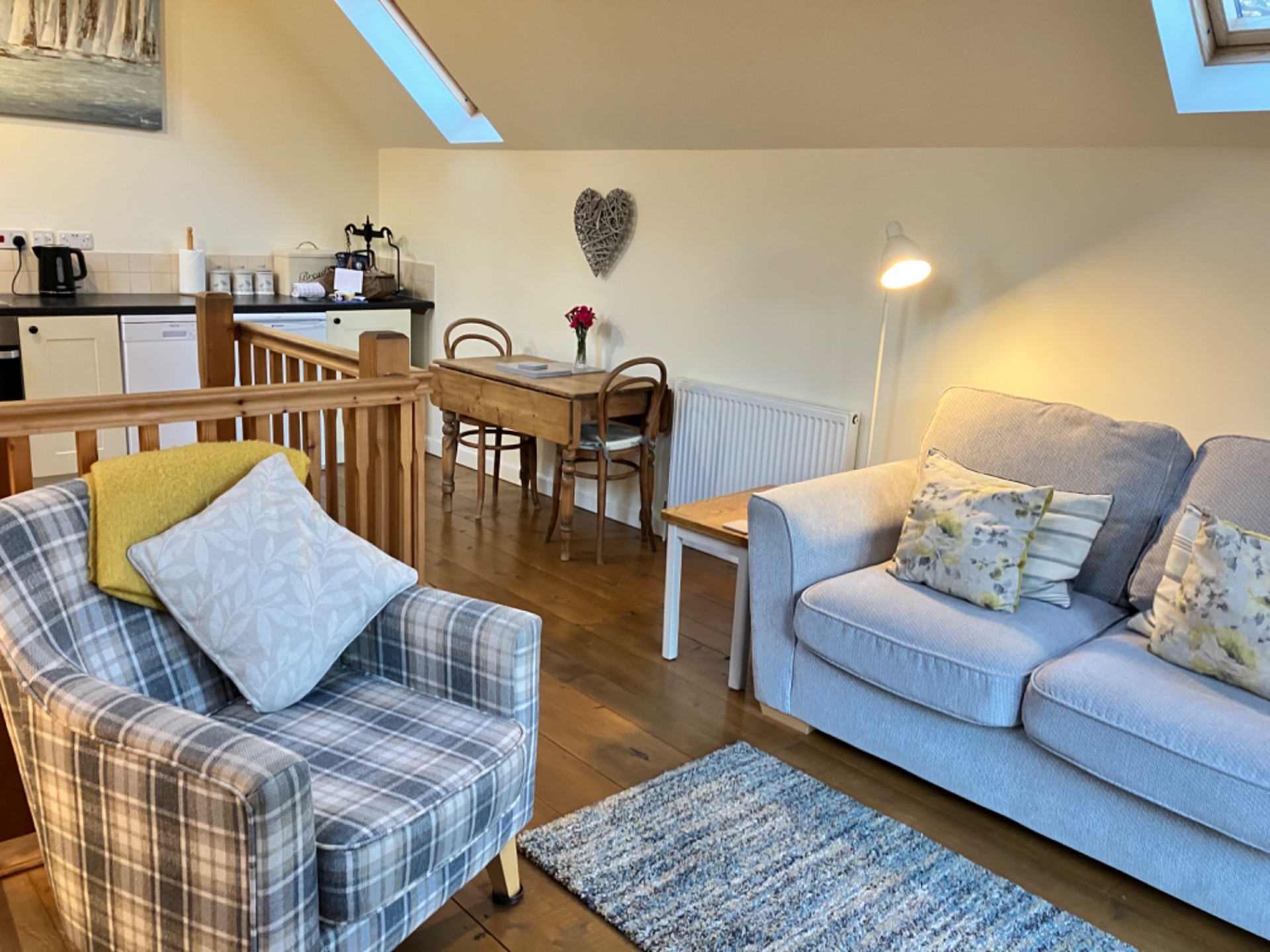 Bright living room with sofa, plaid armchair, dining table, and skylight above kitchen area.